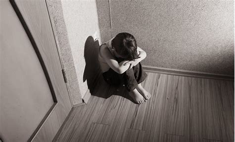 Child sitting in a corner with head down on knees.